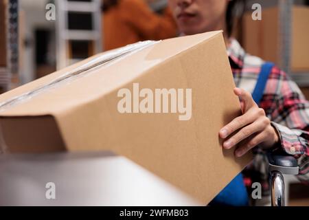 Addetto al magazzino che utilizza una sedia a rotelle tenendo in mano la scatola di cartone. Il gestore degli ordini Storehouse prepara il prodotto per la spedizione, portando il pacco imballato pronto per la spedizione da vicino Foto Stock