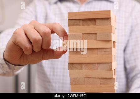 Giocare a Jenga. Uomo che rimuove il blocco di legno dalla torre all'interno, primo piano Foto Stock