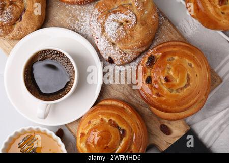 Deliziosi panini con uva passa, zucchero in polvere e tazza di caffè sul tavolo, piatti. Dolci panini Foto Stock