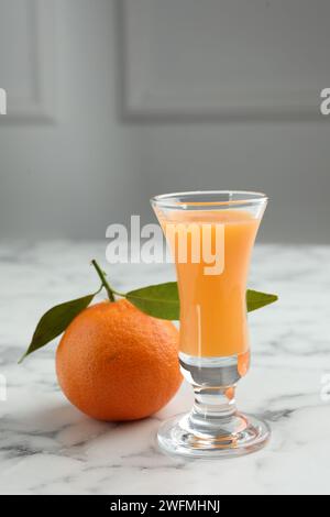 Delizioso liquore al mandarino in bicchierino e frutta fresca su un tavolo in marmo bianco Foto Stock