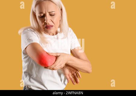 Donna matura che sente dolore al gomito su sfondo giallo Foto Stock