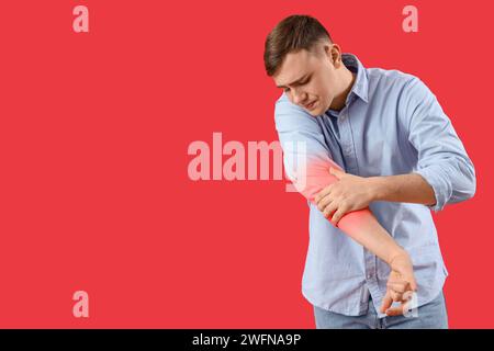 Giovane che sente dolore al gomito su sfondo rosso Foto Stock