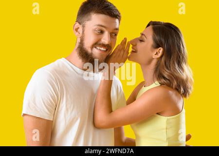 Una giovane donna sussurra all'orecchio del suo ragazzo su sfondo giallo Foto Stock