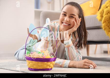 Giovane donna con un cestino di uova di Pasqua sdraiata sul pavimento a casa Foto Stock