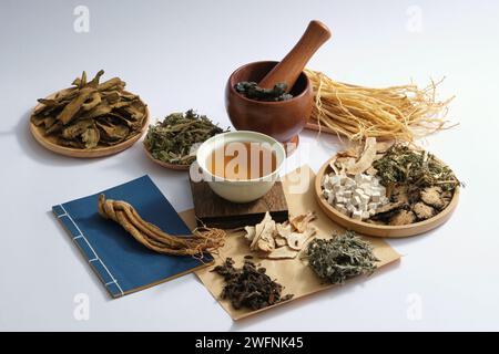 Una ciotola di medicina posta su un podio di legno al centro con molti tipi di erbe esposte intorno. La medicina cinese cura una vasta gamma di disturbi t Foto Stock