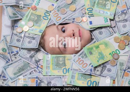 Euro e dollaro. I soldi vincono, buona fortuna. Ragazzo con una faccia divertente in denaro. Ragazzino che sbircia le banconote da un dollaro con occhi sconvolti. Soldi Foto Stock