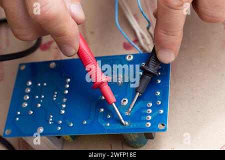 un lavoratore controlla le prestazioni dell'alimentatore utilizzando un multimetro, primo piano. Condensatore di alimentazione. Foto Stock