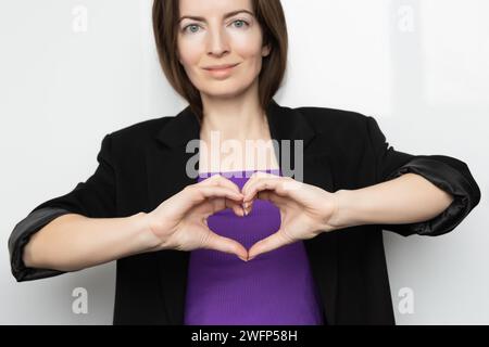 Ispira l'inclusione. Gli Zoomers simboleggiano l'amore. T-shirt viola da donna con cuore al dito. Mano che mostra il cuore. Striscione della giornata internazionale della donna 2024 Foto Stock