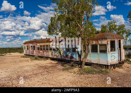 Un tram abbandonato seduto accanto a un albero di gomme in un paesaggio dell'entroterra vicino a Lightning Ridge nel New South Wales, Australia. Foto Stock