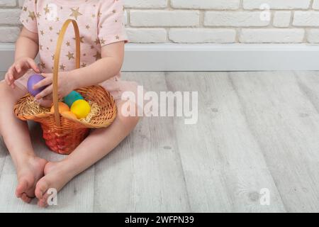 Ragazza irriconoscibile seduta sul pavimento con uova di Pasqua colorate nel cestino di vimini a casa Foto Stock