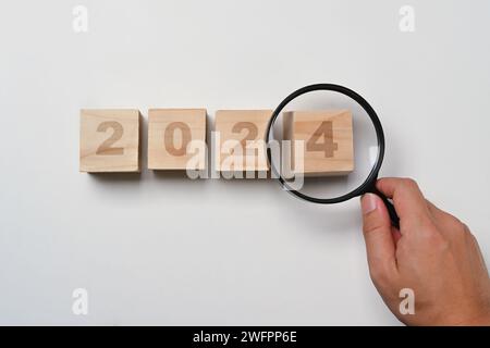 Lente d'ingrandimento con mano su cubi di legno con numero di 2024 anni. Obiettivo di Capodanno e concetto di risoluzione Foto Stock