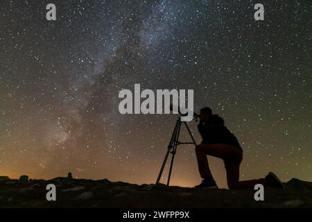 un uomo guarda attraverso un telescopio su un treppiede al cielo stellato Foto Stock