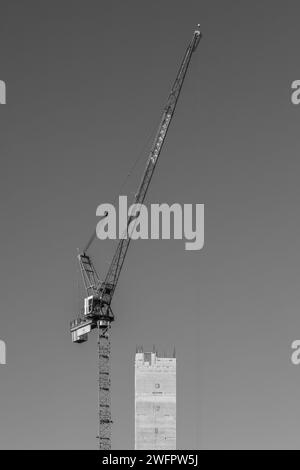 Immagine ritratto in bianco e nero di una gru a torre sopra la torre del nucleo di cemento di uno sviluppo edilizio Victoria a Manchester, Regno Unito. Foto Stock