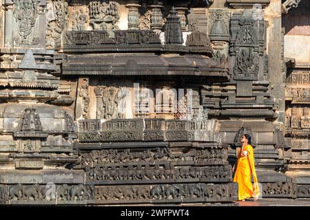 Belur, Karnataka, India - 9 gennaio 2023: Una donna indiana che indossa un sari arancione brillante e si gode le antiche sculture del tempio di Chennakeshava. Foto Stock