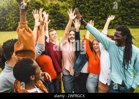 Esuberante e diversificato gruppo di amici che si alzano la mano per festeggiare, godendosi una vivace riunione all'aperto. Foto Stock