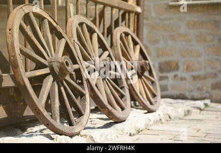 Tre vecchie ruote in legno per carri trainati da cavalli appoggiati in prospettiva a un muro di legno Foto Stock