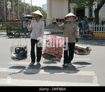 02/07/2014 - Saigon, Vieatnam: Due venditori ambulanti vietnamiti che bilanciano merci su pali sulle spalle, una vista comune nelle vivaci strade Foto Stock