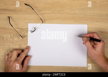 Spazio di lavoro creativo: Vista dall'alto verso il basso delle mani che disegnano il white paper con la penna a sfera su un tavolo di legno - concetto minimalista di Office con spazio per la copia. Foto Stock