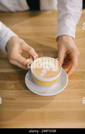 Le mani del barista hanno in mano un delizioso cappuccino. Primo piano, vista dall'alto. Foto Stock