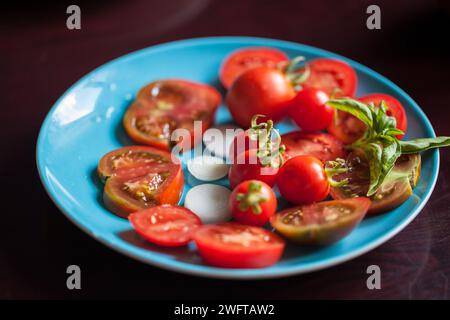 Colorato mix di pomodori ciliegini appena raccolti con basilico sul piatto blu Foto Stock