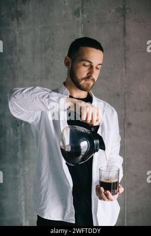 Bel barista che versa del caffè gocciolante appena fatto in una tazza di vetro. Preparazione del metodo alternativo per il caffè. Foto Stock
