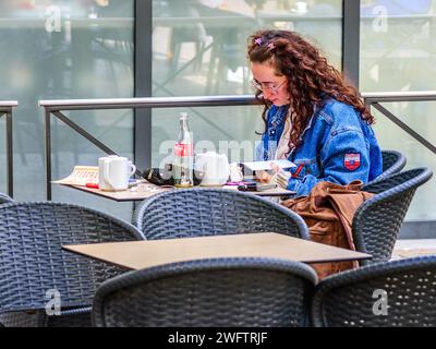 Giovane donna con lunghi capelli ondulati di auburn lettura al tavolo del caffè - Tours, Indre-et-Loire (37), Francia. Foto Stock