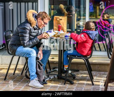 Padre che controlla lo smartphone con un figlio giovane seduto al tavolo del caffè all'aperto - Tours, Indre-et-Loire (37), Francia. Foto Stock