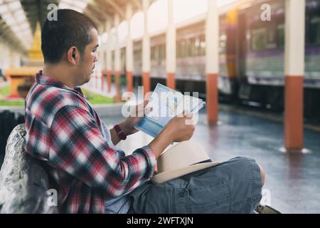 Un viaggiatore giovane con mappa seduto in stazione scegliere dove viaggiare. Concetto di avventura di viaggio backpackers in treno. Foto Stock