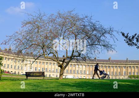 In un giorno di primavera di sole, un uomo viene ritratto spingendo un passeggino davanti al famoso Royal Crescent di Bath, Somerset, Inghilterra, Regno Unito. Foto Stock