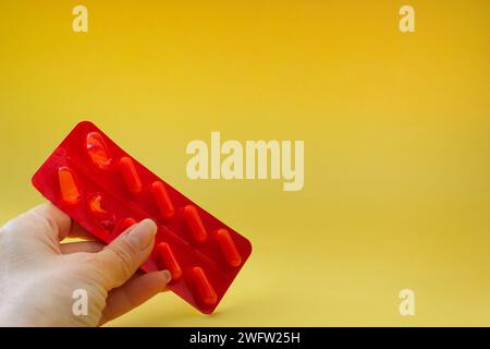 la mano femminile tiene medicinali isolati su sfondo giallo, offre farmaci, aiuta Foto Stock