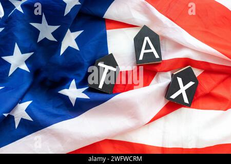 Vista dall'alto dei cubi di legno con TASSA DI testo sulle banconote in dollari americani sulla bandiera americana. Concetto di TASSE e IVA Foto Stock