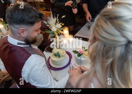 Augusta, Baviera, Germania - 19 gennaio 2024: La giovane sposa e lo sposo tagliano insieme la torta al loro matrimonio *** Junges Brautpaar schneidet zusammen bei der Hochzeit die Hochzeitstore an Foto Stock