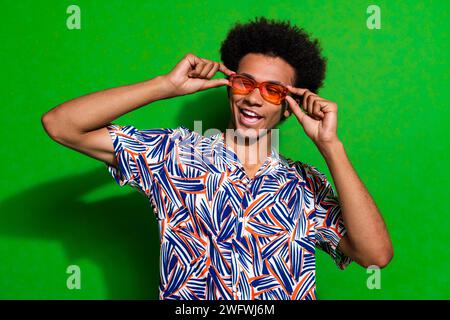 Foto di un ragazzo stravagante impressionato che indossa una camicia stampata mani braccia occhiali scuri che sembrano spazi vuoti sfondo di colore verde isolato Foto Stock