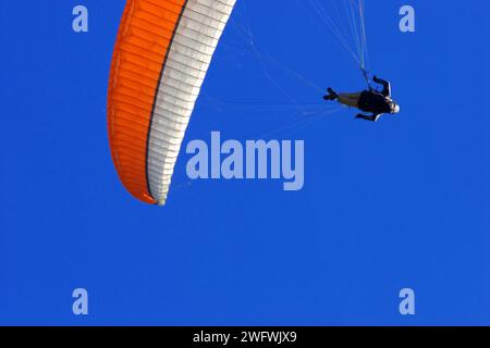 un parapendio con un baldacchino bianco e arancione nel cielo blu Foto Stock