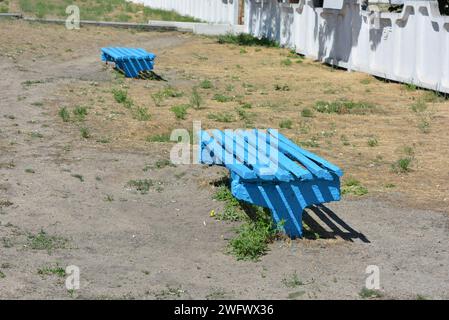 Le solite panchine in legno sono dipinte di blu e si trovano non lontano dalla fermata ferroviaria. Foto Stock