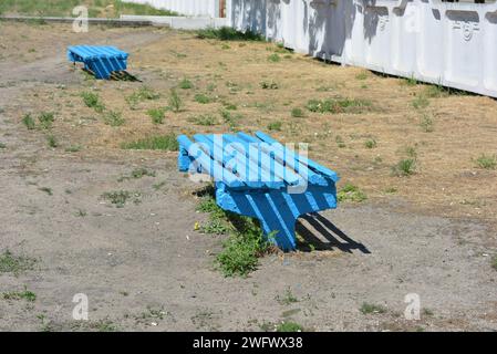 Le solite panchine in legno sono dipinte di blu e si trovano non lontano dalla fermata ferroviaria. Foto Stock