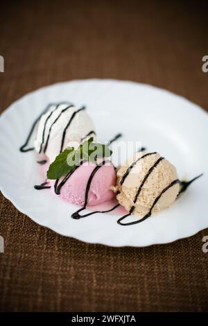 Un angolo elevato di cucchiai di delizioso gelato fatto in casa serviti in una ciotola e conditi con sciroppo di cioccolato per primo piano Foto Stock