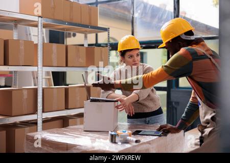 I colleghi del magazzino preparano i pacchi dei clienti utilizzando scatole di cartone, controllano i dettagli di consegna sul computer portatile nel magazzino. Team diversificato che lavora al report inventario merchandising Foto Stock