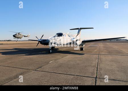 Un aereo C-12 Huron è parcheggiato sulla rampa, mentre un elicottero UH-72 Lakota taxi presso il Cairns Army Airfield il 31 gennaio 2024. Il C-12 è assegnato al distaccamento 1, compagnia B, 1st Battalion, 228th Aviation Regiment, U.S. Army Reserve, ed è di stanza a Fort Novosel, Alabama, sede del U.S. Army Aviation Center of Excellence. Foto Stock