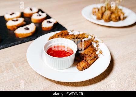 Tender di pollo croccanti dorati serviti su un piatto bianco con salsa al peperoncino dolce, perfetti per uno spuntino salato o un antipasto. Foto Stock