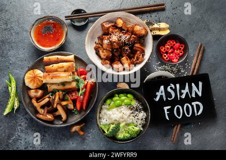 Teriyaki di pollo su sfondo scuro con salse, riso, verdure e semi di sesamo. Cibo asiatico. Vista dall'alto. Foto Stock