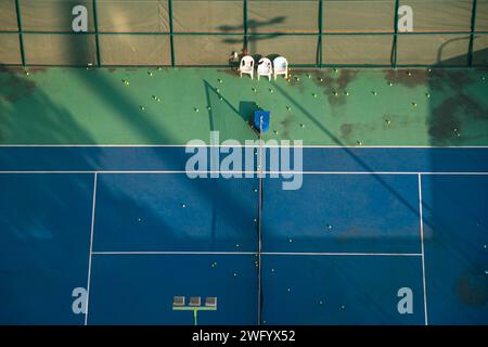 Vista aerea di un campo da tennis immerso nella calda luce del sole invernale, con palle da tennis sparse Foto Stock