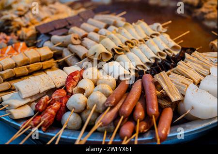 Gli spiedini di carne cinesi assortiti dai colori vivaci illuminati da luci calde, con sapori deliziosi Foto Stock