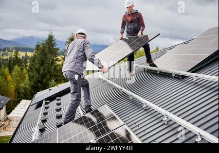 Tecnici professionisti che trasportano batterie solari fotovoltaiche. Ingegneri che installano pannelli solari su un tetto di casa. Risorse alternative e concetto di energia verde. Foto Stock