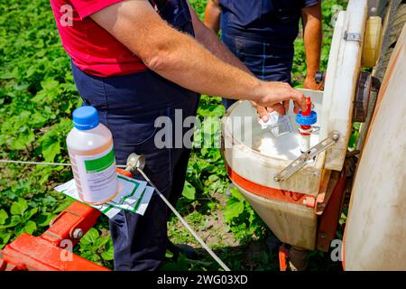 Le mani dell'agricoltore durante la preparazione, miscelando i prodotti chimici in scala adeguata da diversi sacchetti e bottiglie di plastica, riempiendo il serbatoio dell'irroratrice. Foto Stock