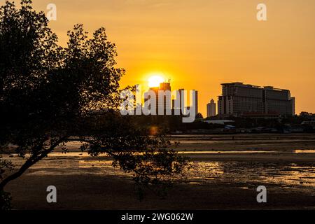 Splendida vista del tramonto serale dietro gli edifici sagomati di Pattaya, Thailandia, con il sole riflesso sull'acqua in primo piano Foto Stock