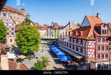 La piazza Tiergärtnertor di Norimberga, in Germania, è fiancheggiata da edifici in legno e caffè sul marciapiede, dominati dalle torri del castello. Foto Stock