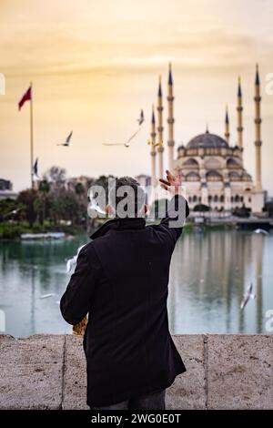 Adana, Turkiye - 25 gennaio 2024: Uomo che dà da mangiare ai gabbiani con pezzi di pane sullo storico Taskopru, il Ponte di pietra ad Adana, Turkiye. Foto Stock