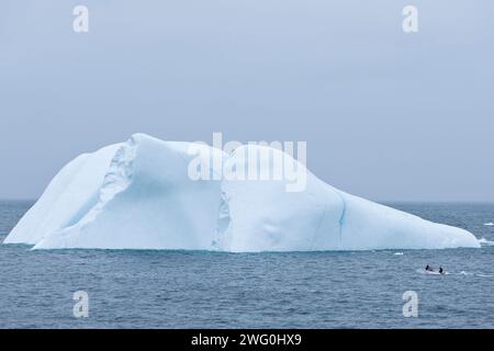 Un piccolo peschereccio passa davanti a un iceberg sulla costa orientale della Groenlandia vicino alla città di Ammassalik. Foto Stock