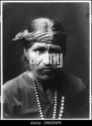 Il cantante ridendo, c1905. Uomo Navajo, ritratto della testa e delle spalle, rivolto verso la parte anteriore, indossa una collana e un cerchietto. Foto Stock